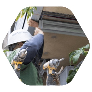Worker in hardhat installs or repairs outdoors, with power drills visible in front.