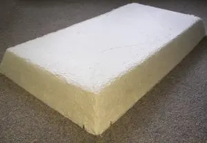 A large rectangular block of white pulp, reminiscent of an FF130-2x4 Fire Rated Troffer Cover from Tenmat USA, is pressed against a carpeted floor.