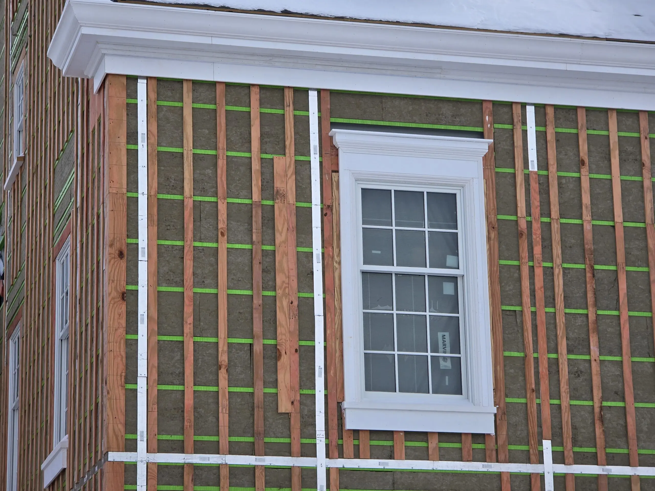 House under construction with exposed insulation and a window framed in white trim.