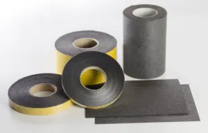 Four rolls and two sheets of black adhesive material, some partially unrolled, on a white surface.