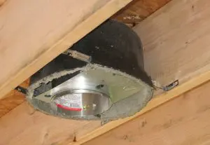 A recessed light housing with recessed light covers installed between wooden ceiling joists.