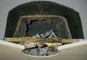 A helmet with a large hole and damaged metal inside, possibly where high hat covers once offered protection, shows signs of severe impact or penetration.