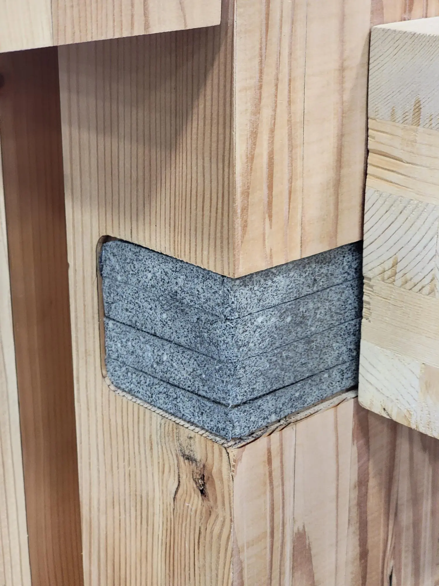 Close-up of a wooden joint with a gray concrete or stone block set into the wood.