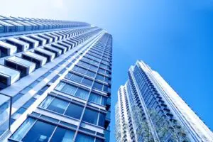 Two modern skyscrapers with glass windows viewed from below against a bright blue sky.