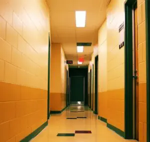 Empty hallway with yellow and orange walls, green door frames, and bright overhead lights.