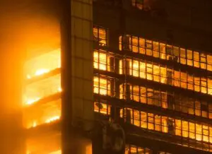 Flames engulf multiple floors of a building at night, shining through broken windows.