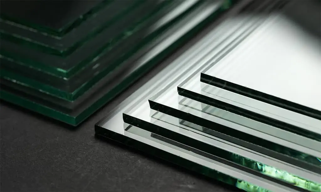 Clear glass sheets stacked with green edges on a dark surface.