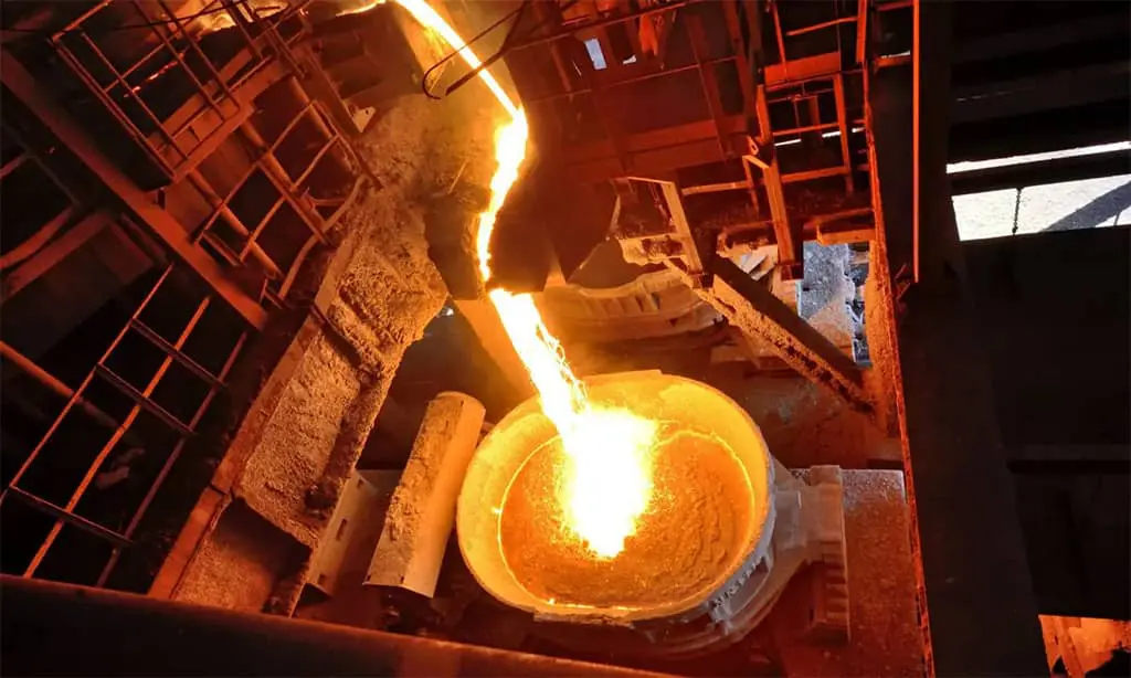 Molten metal pours from a furnace into a large container at a foundry.