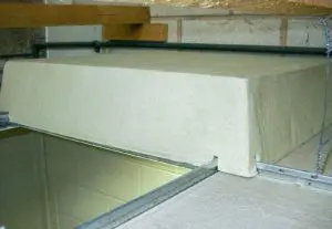 A rectangular block of insulating material rests above a suspended ceiling in a building, positioned near a troffer light cover.