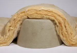 A thick layer of yellow insulation wool draped over a gray, dome-shaped recessed light insulation fixture against a plain background.