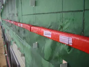 Close-up of a building wall with green weather barrier, fire barrier, and red flashing, all marked with installation instructions.
