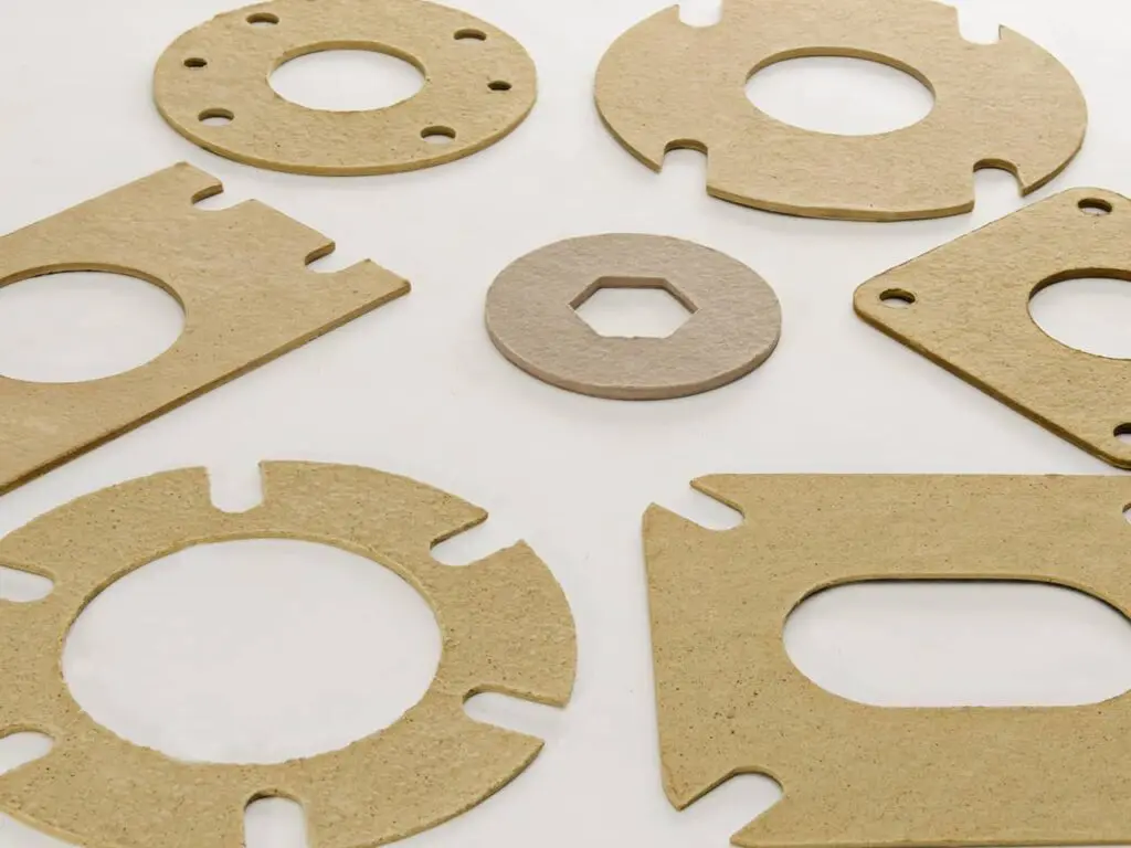Various flat cardboard gaskets with cut-outs, arranged on a white surface.