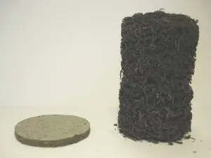 A flat gray disk, possibly part of a 2 hour fire rated ceiling system, sits beside a tall, curly, black cylindrical object on a plain background.