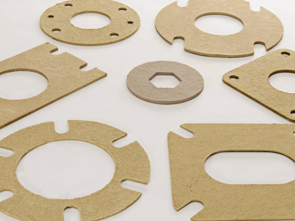 Various flat cardboard gaskets with cut-outs, arranged on a white surface.