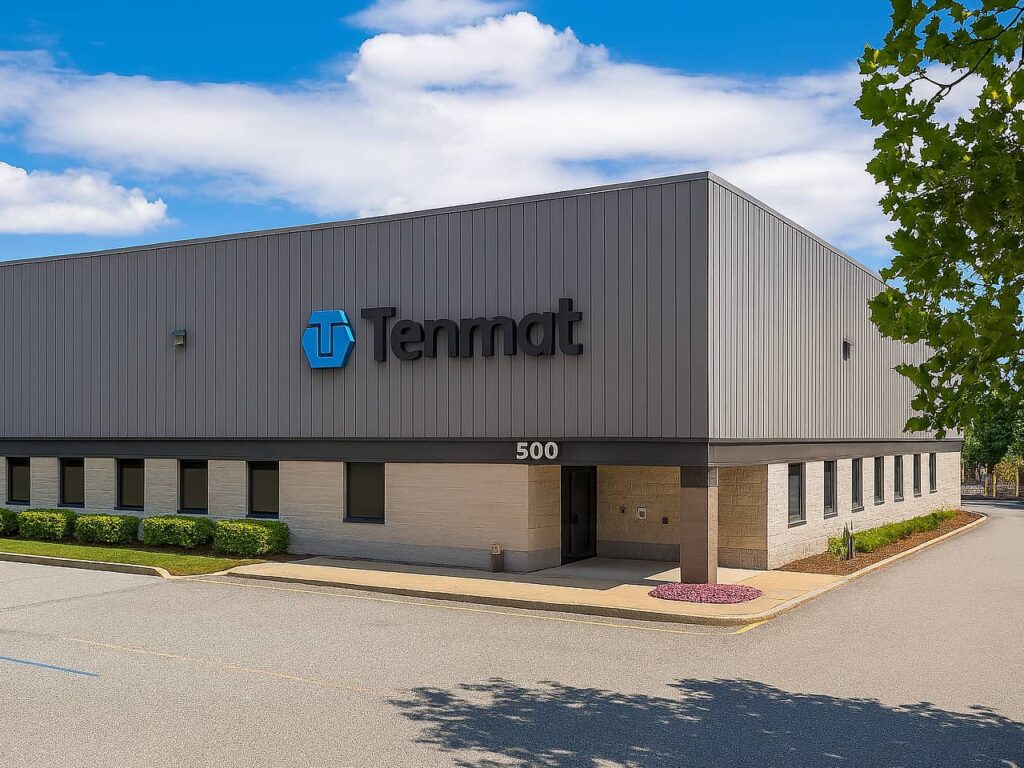 Grey industrial building with Tenmat sign and 500 on front, set against a blue sky.